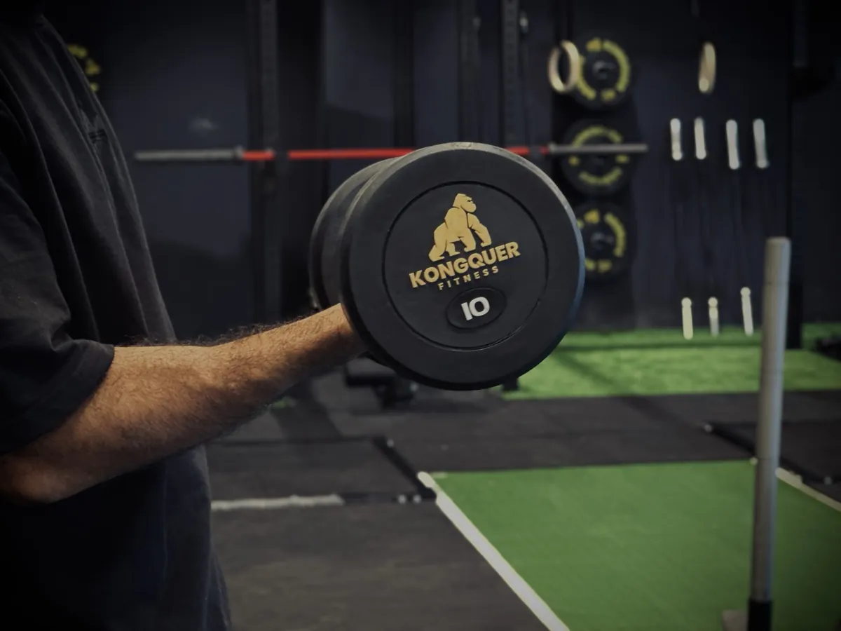 Athlete gripping a branded Kongquer 10kg dumbbell on the floor